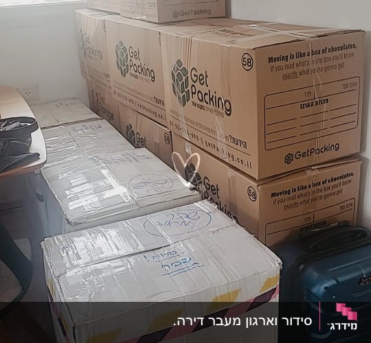 קופסאות קרטון מסודרות ליד מזוודה כחולה